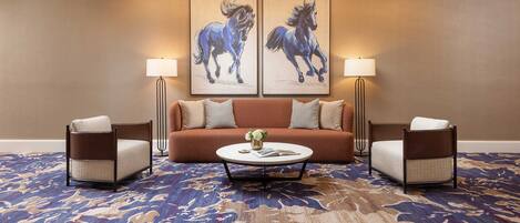 A hotel room with a sofa, two armchairs, a coffee table, and two wall-mounted lamps.