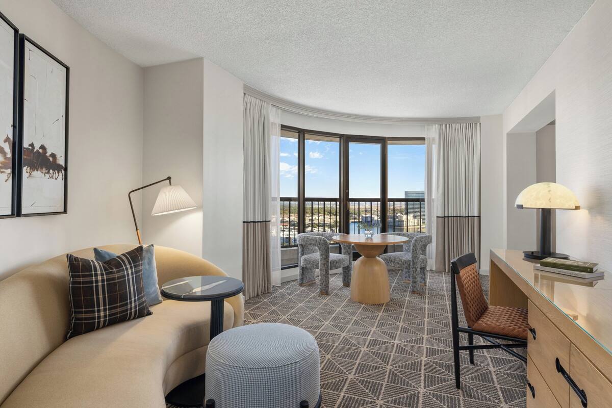 A modern hotel room with a curved ceiling, a sofa, a round table, and a dining area with chairs.
