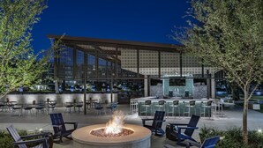 An outdoor seating area with a fire pit, chairs, and a bar area with a counter and stools. - Omni Las Colinas Hotel (Irving)