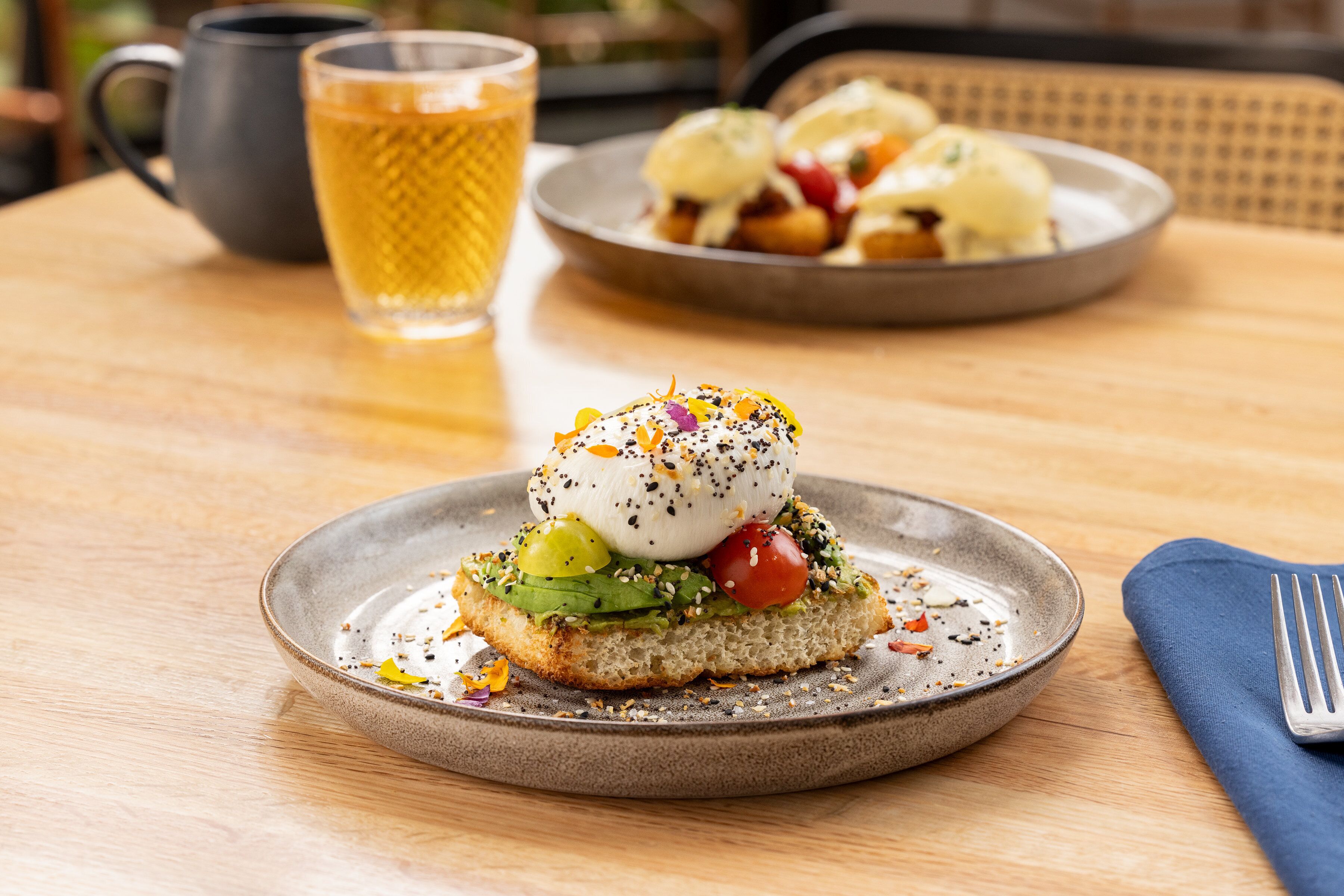 A breakfast dish with a poached egg, avocado, and tomatoes on toast, served on a ceramic plate.