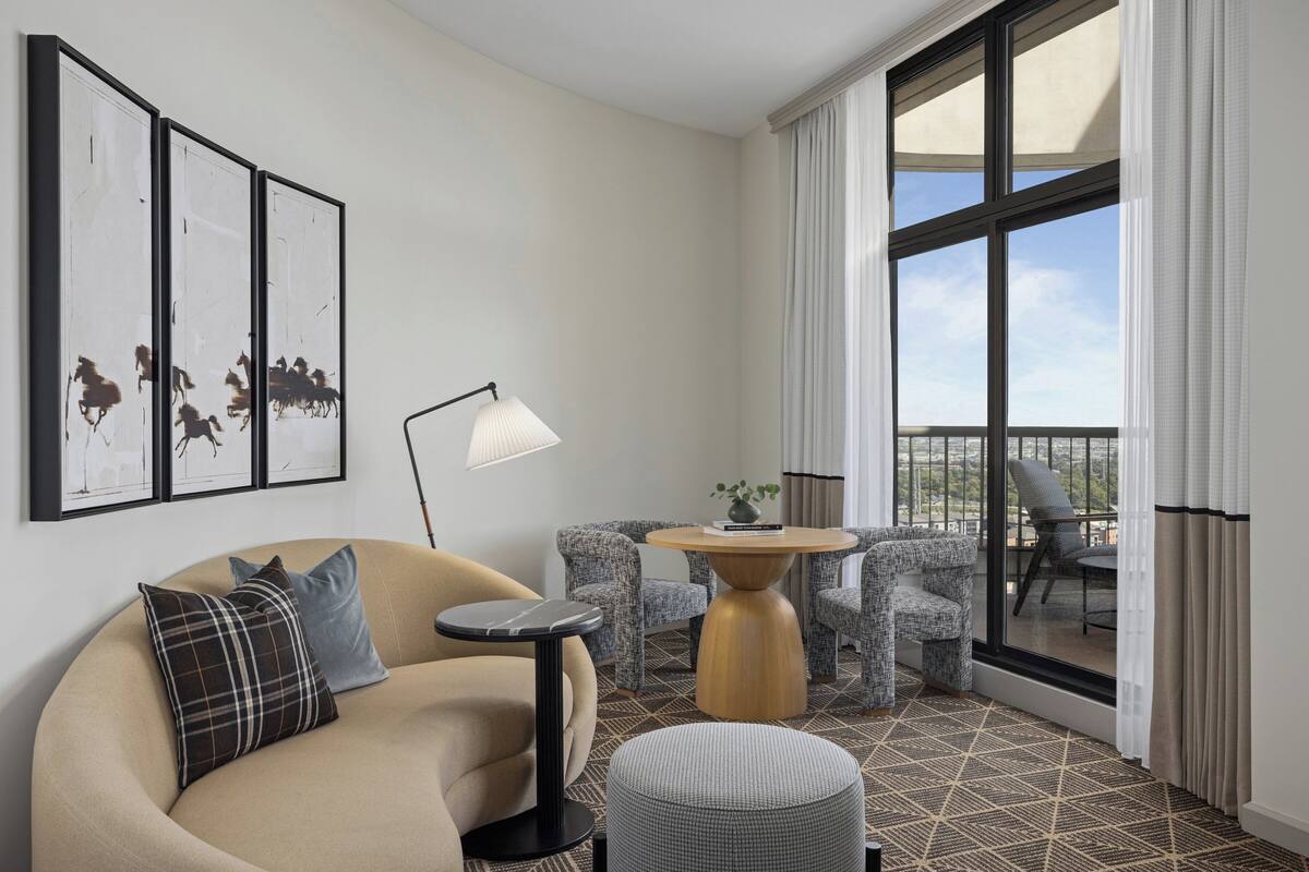 A modern hotel room with a sofa, two armchairs, a small round table, and a balcony with a view.