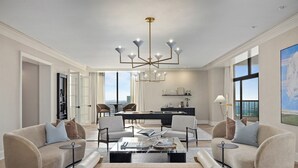 A spacious living room with a modern chandelier, comfortable seating, a dining area, and large windows offering views. - Omni Las Colinas Hotel (Irving)