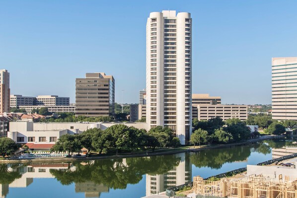 A high-rise building with a modern design, surrounded by trees and a body of water reflecting the structure. - Omni Las Colinas Hotel (Irving)