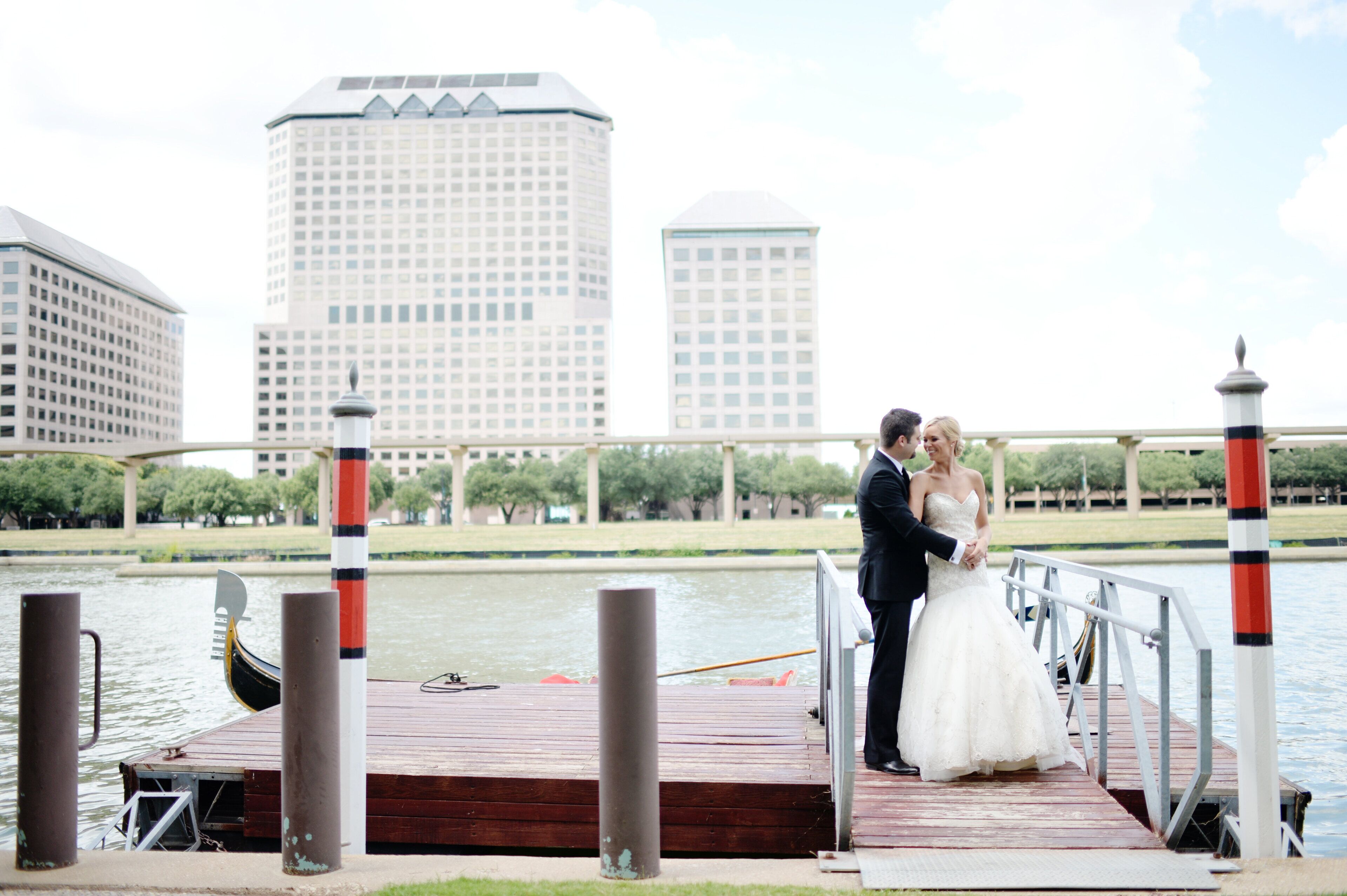 A couple on a wooden dock with a cityscape in the background.
