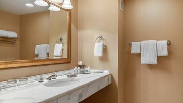 Une salle de bain avec un lavabo en marbre, plusieurs porte-serviettes, un grand miroir et un espace douche.