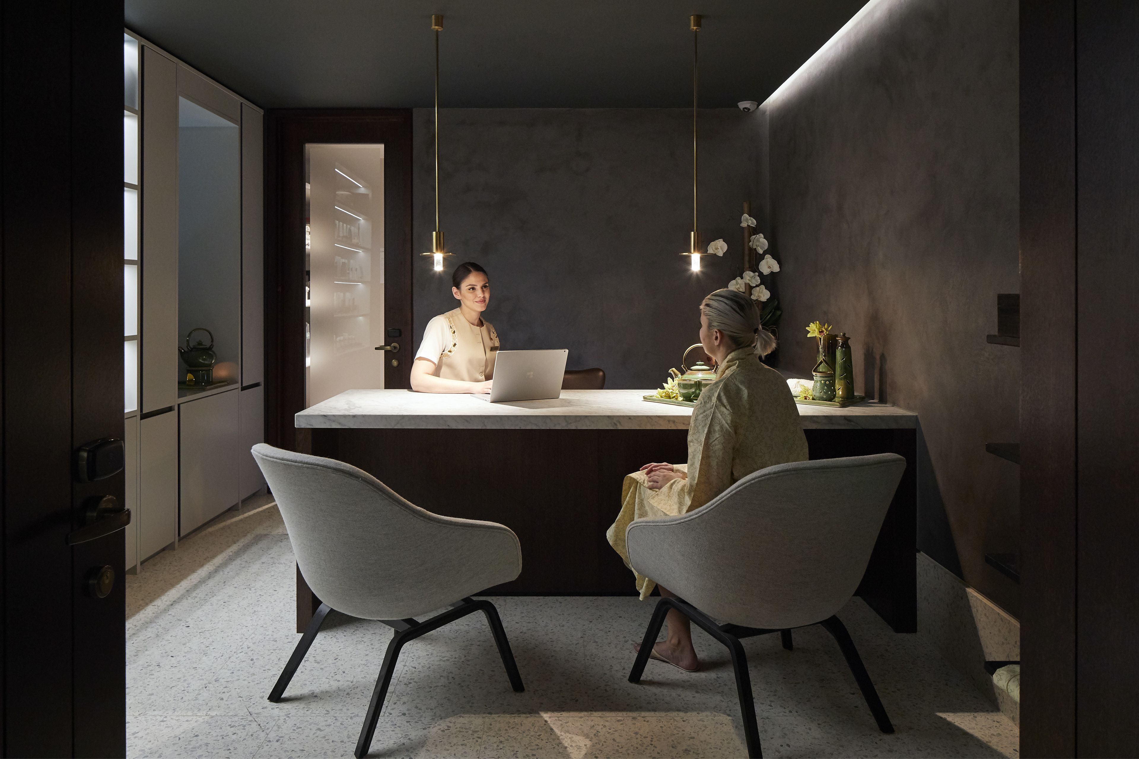 Une cuisine moderne dotée d’un plan de travail en marbre, de deux chaises et de luminaires suspendus.