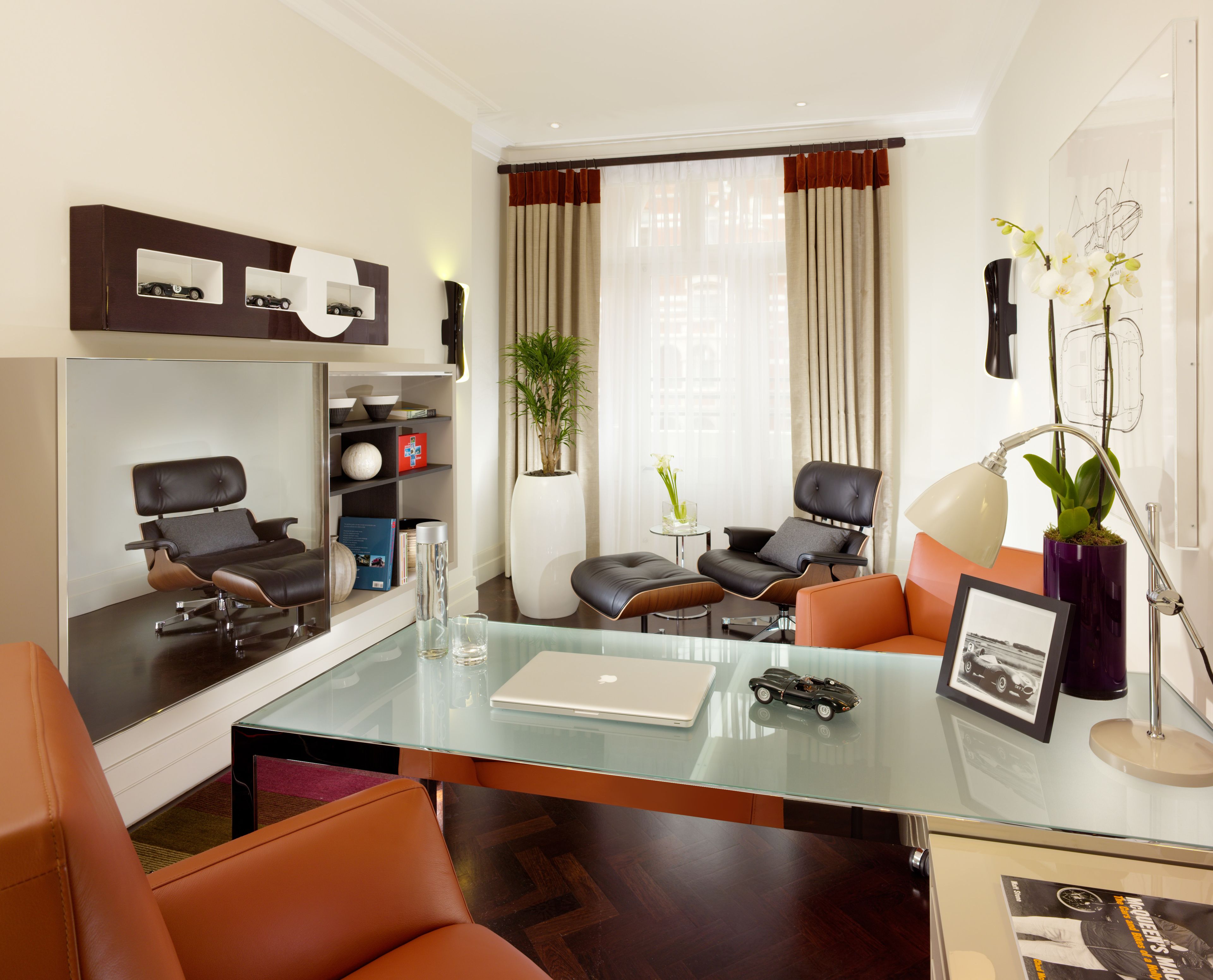 A modern living room with a glass coffee table, leather sofas, a laptop, and a bookshelf with decorative items.