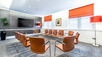 A conference room with orange chairs, a flat-screen TV, and a red lamp.