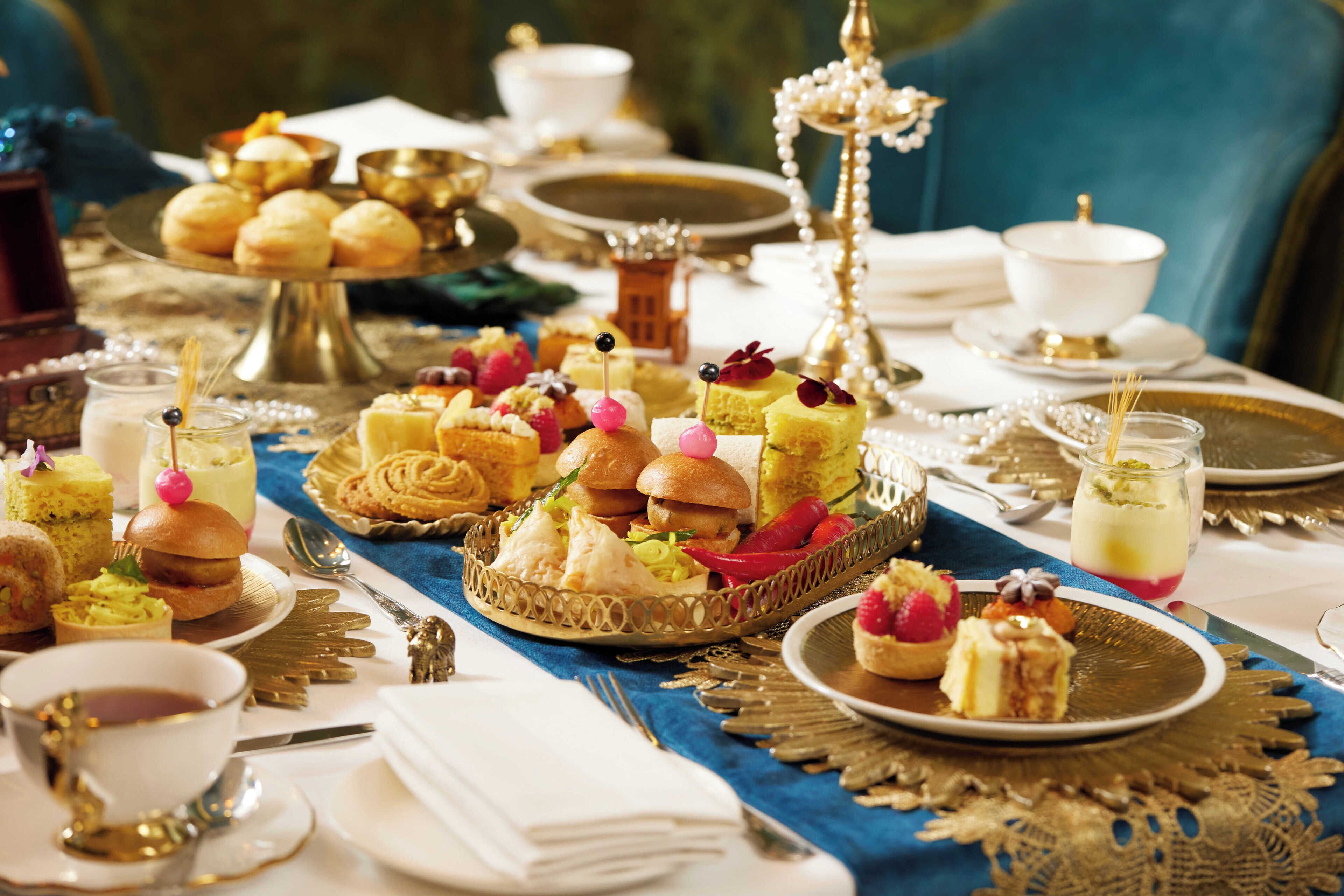 A table set with various desserts and pastries, including cakes, cupcakes, and fruit tarts, arranged on ornate golden trays and plates.