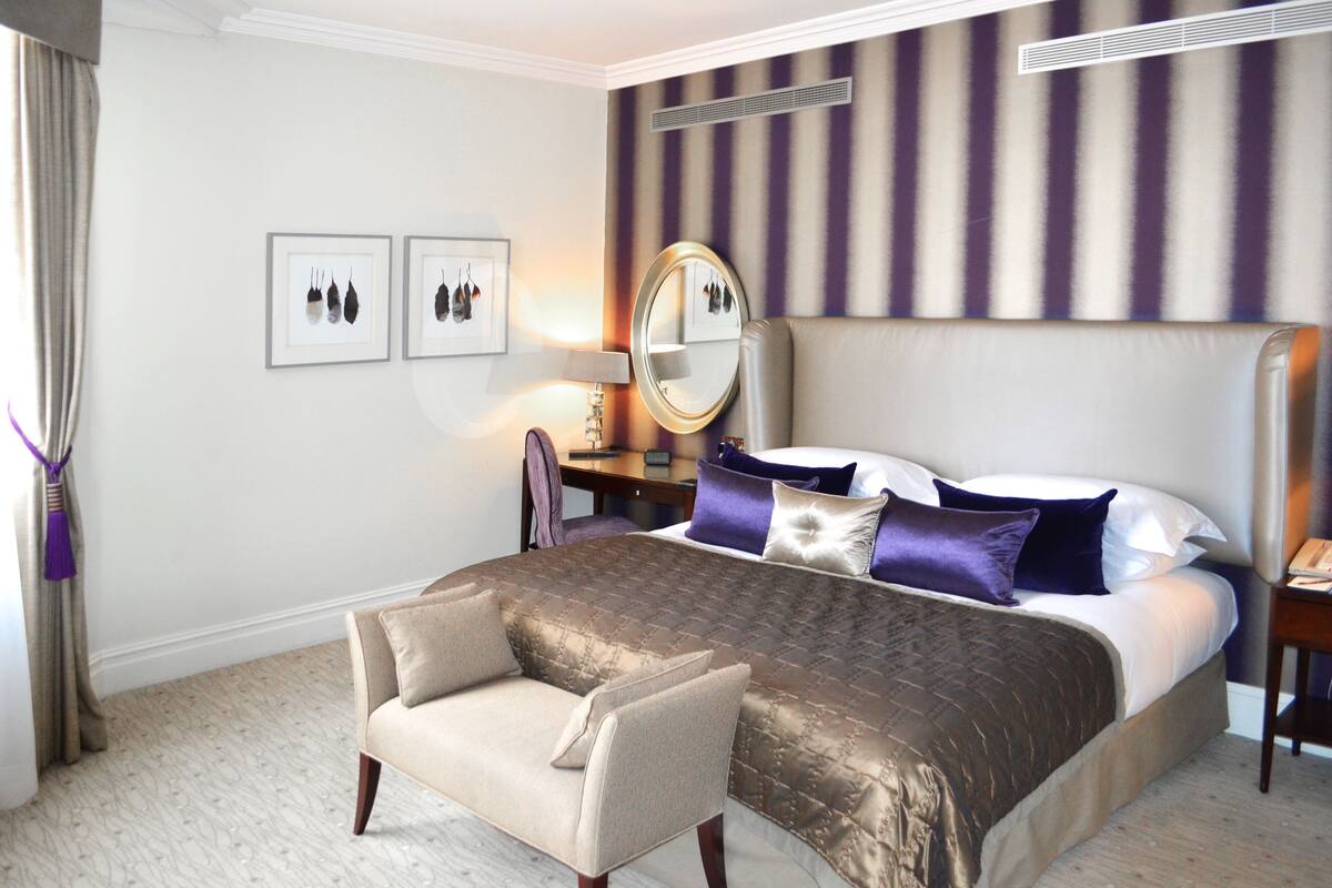 Une chambre d’hôtel avec un grand lit, une chaise, une table de chevet, un miroir et un tableau au mur.