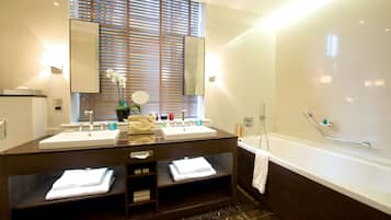 A bathroom with two sinks, a large mirror, a bathtub, and a window with blinds.