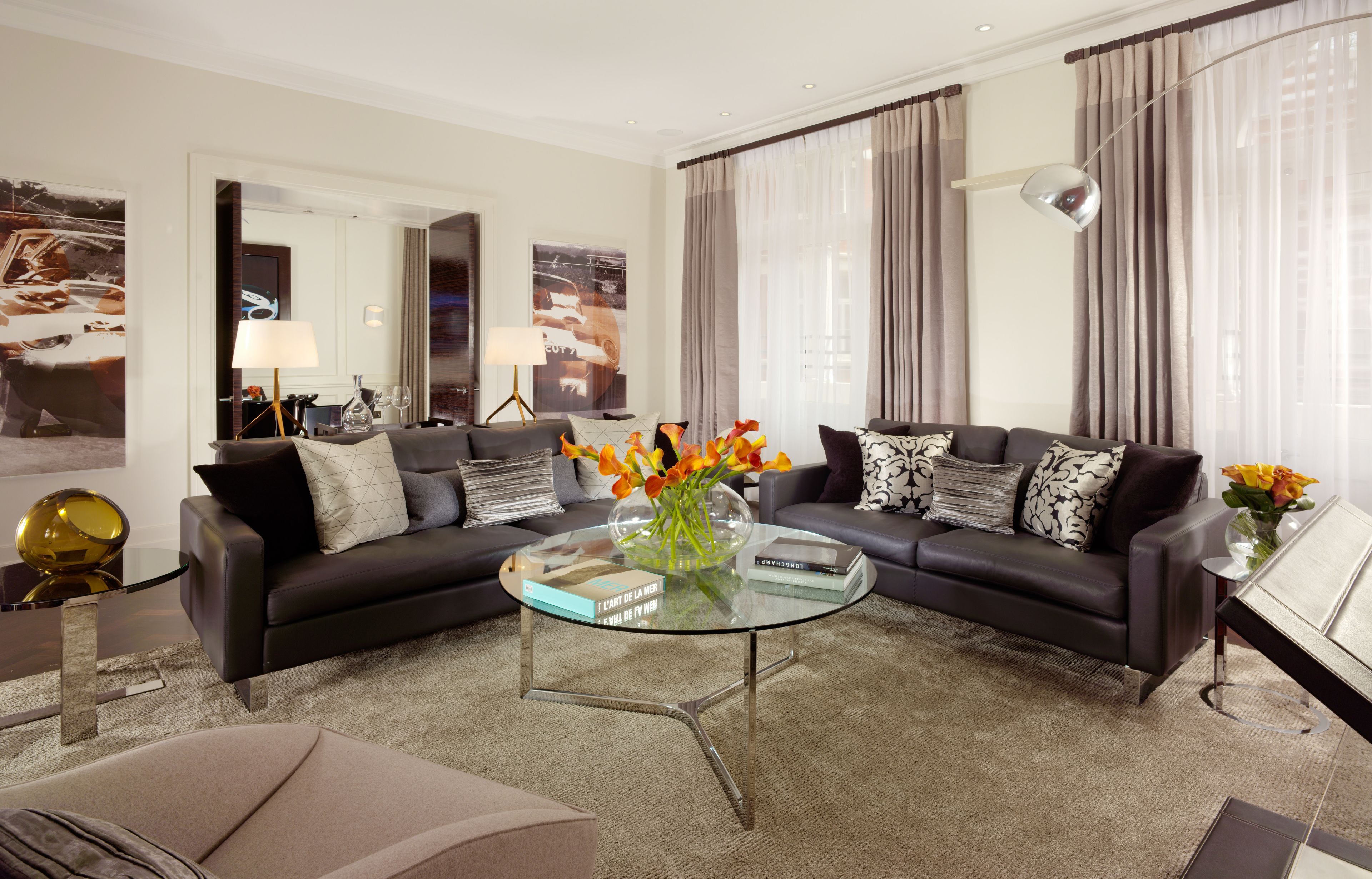 A modern living room with a black leather sofa, a glass coffee table, and a vase with flowers.