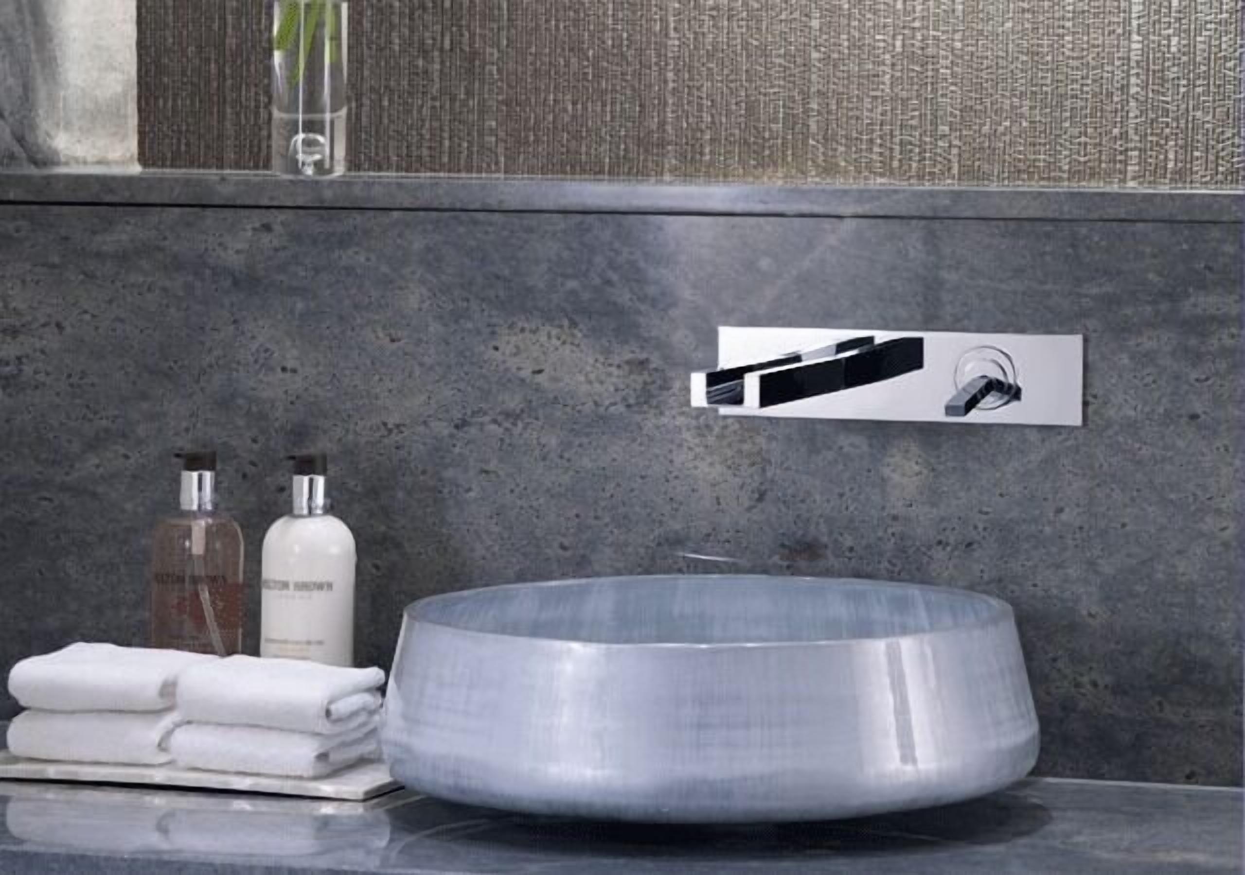 A modern bathroom with a large, round, metallic sink, a towel rack with folded towels, and two bottles of hand soap.