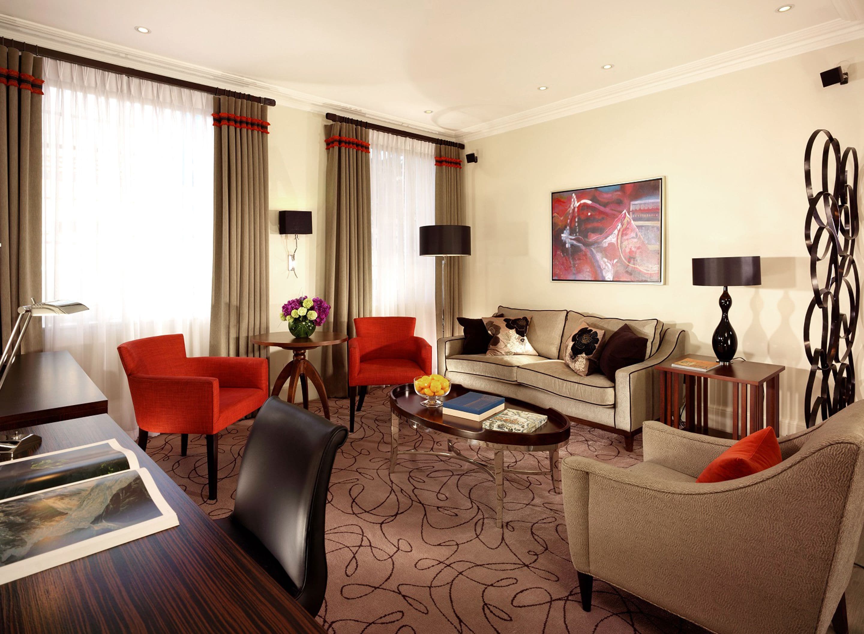 Habitación de hotel luminosa con sofá, dos sillones, una mesa de centro, un escritorio y una lámpara.