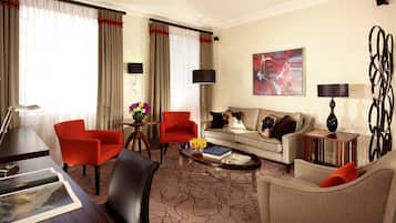 Habitación de hotel luminosa con sofá, dos sillones, una mesa de centro, un escritorio y una lámpara.