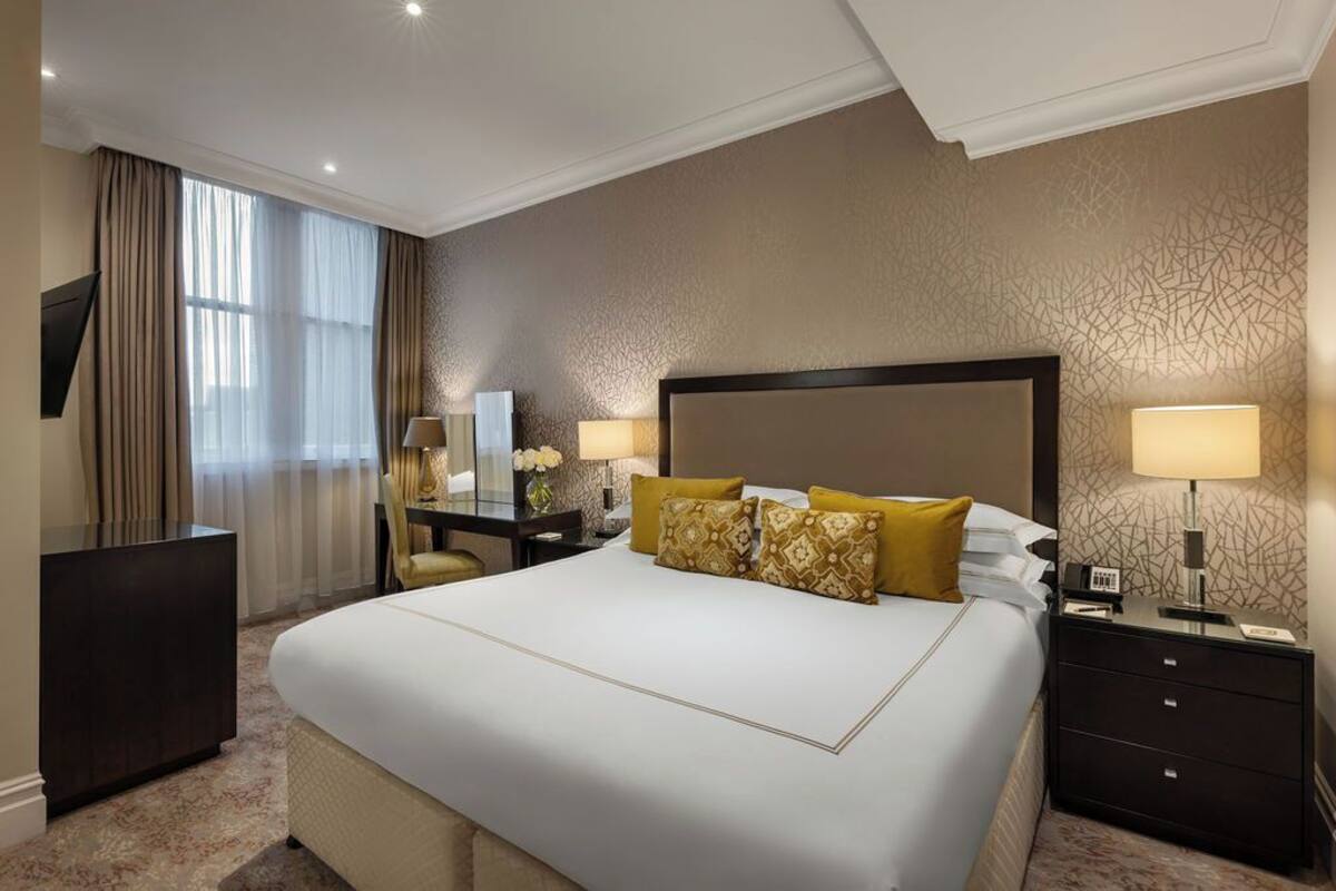 Une chambre d’hôtel avec un grand lit, deux tables de chevet avec des lampes, un bureau avec une chaise et un téléviseur fixé au mur.