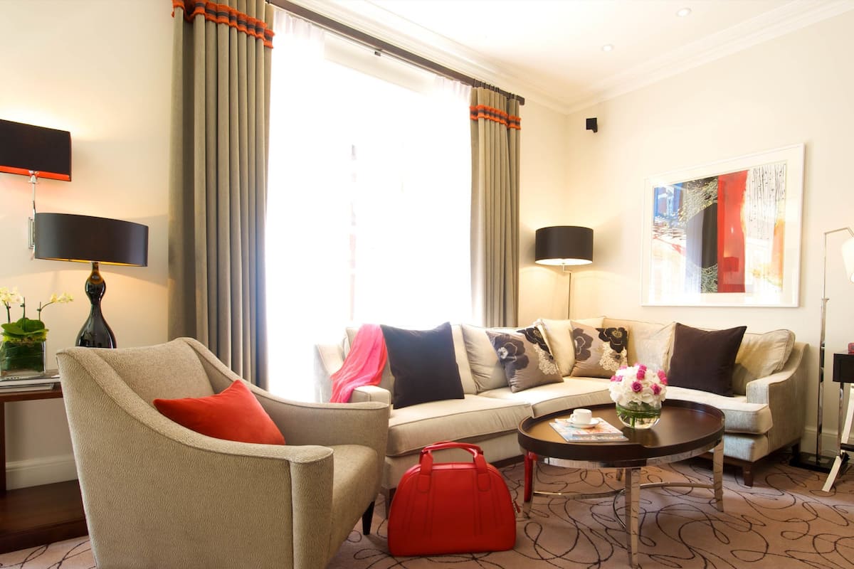 Une chambre d’hôtel avec un canapé, un fauteuil, une table basse et un sac à main rouge posé sur le sol.