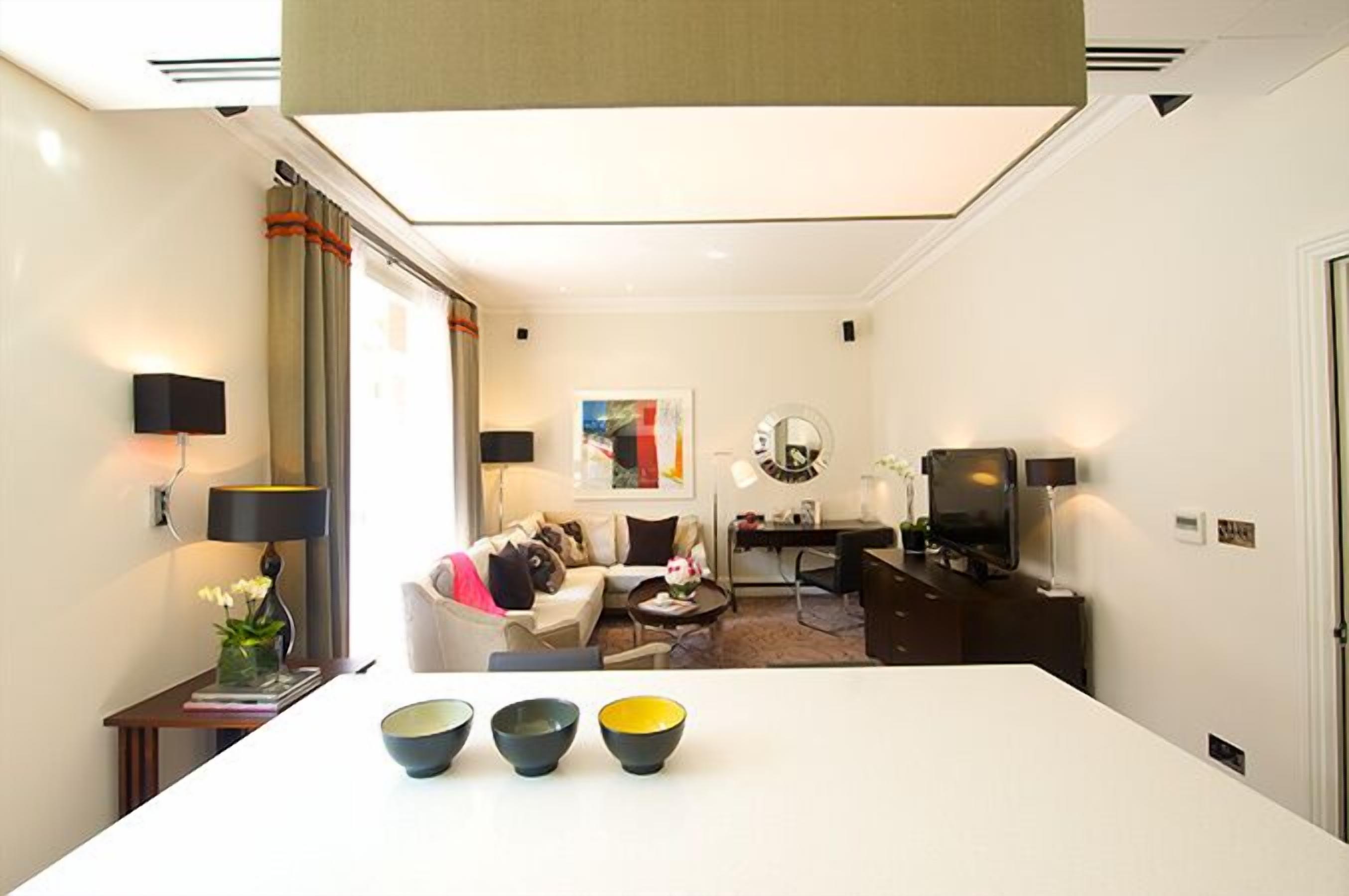 A modern hotel room with a white dining table, a sofa, a TV, and a desk.