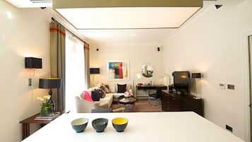 A modern hotel room with a white dining table, a sofa, a TV, and a desk.