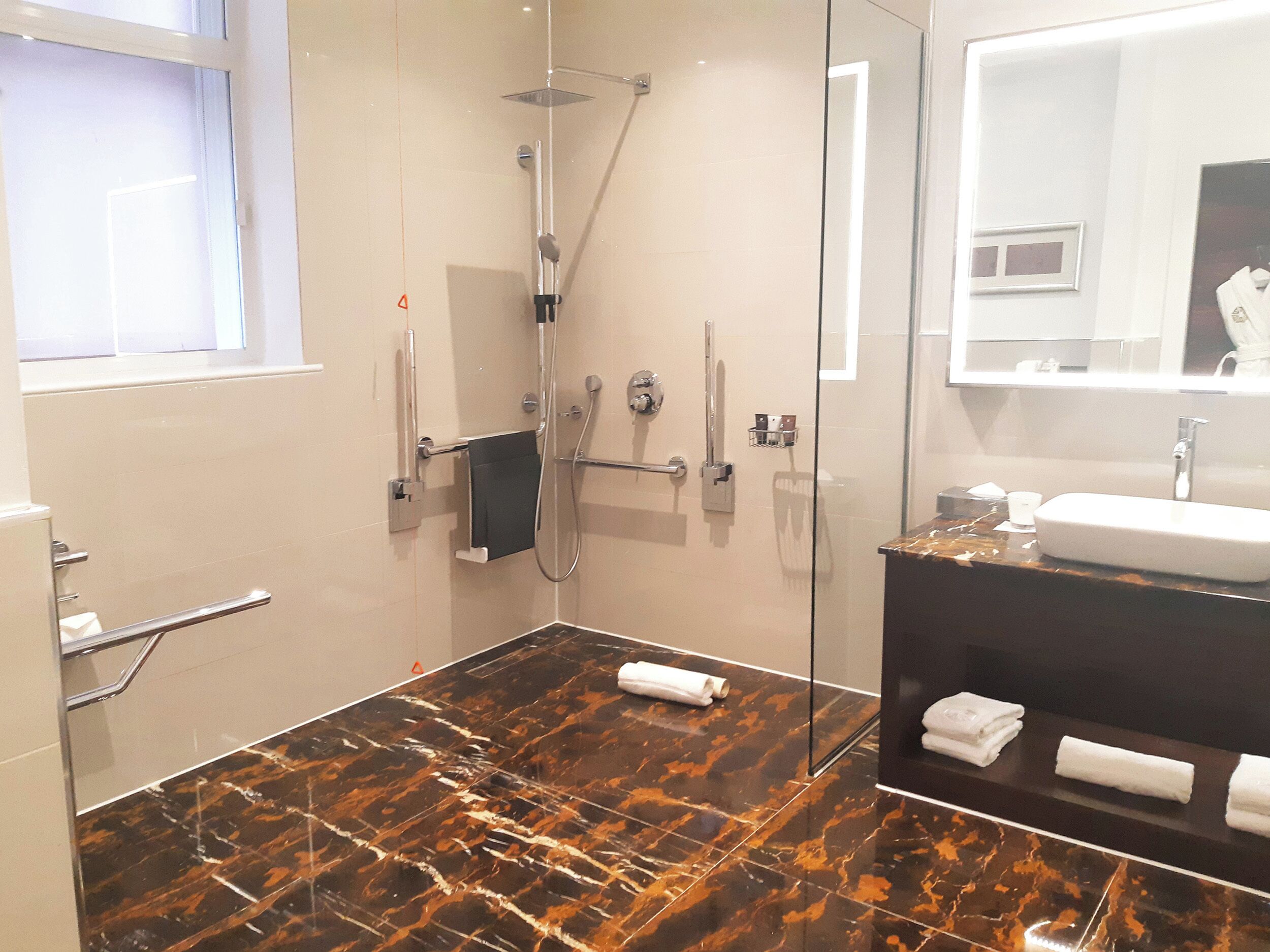 A modern bathroom with a glass shower enclosure, a marble-tiled floor, a sink with a mirror, and a towel rack.