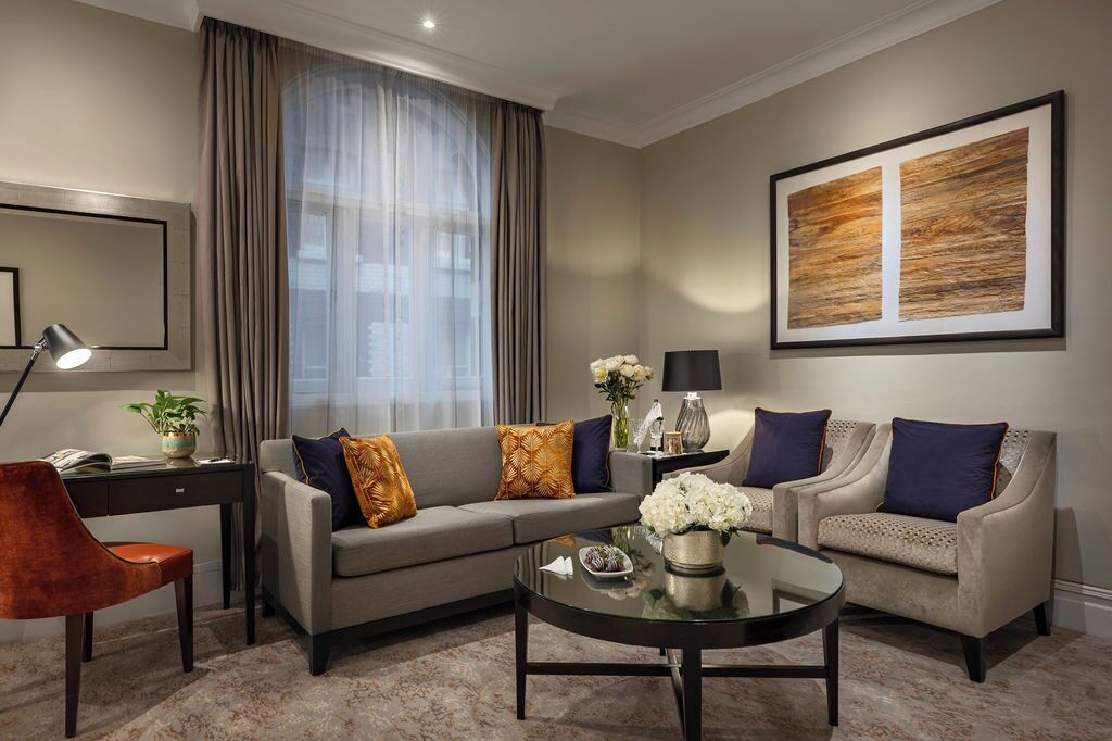 A modern living room with a grey sofa, two armchairs, a coffee table, and a large abstract painting on the wall.