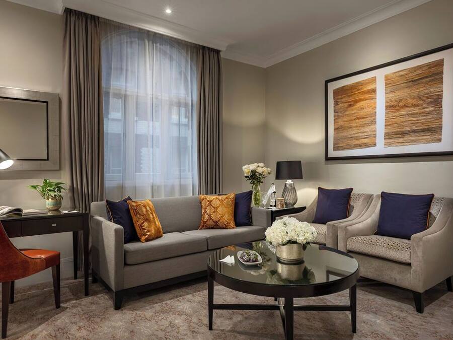 A modern living room with a grey sofa, two armchairs, a coffee table, and a large abstract painting on the wall.
