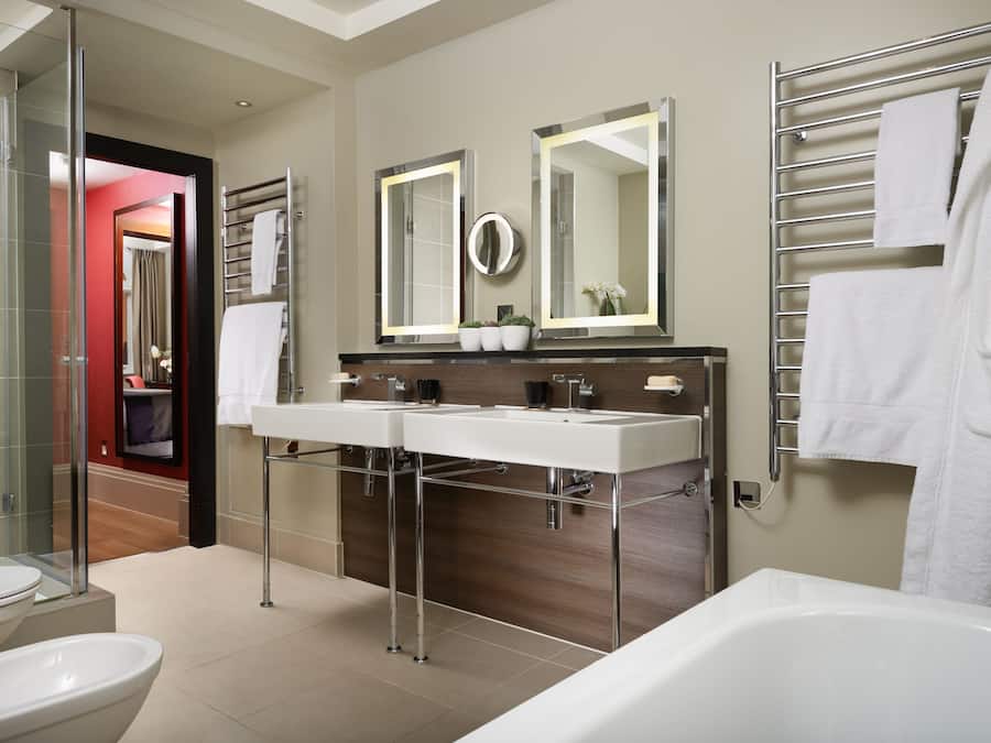 A modern bathroom with two sinks, a large mirror, and a bathtub.