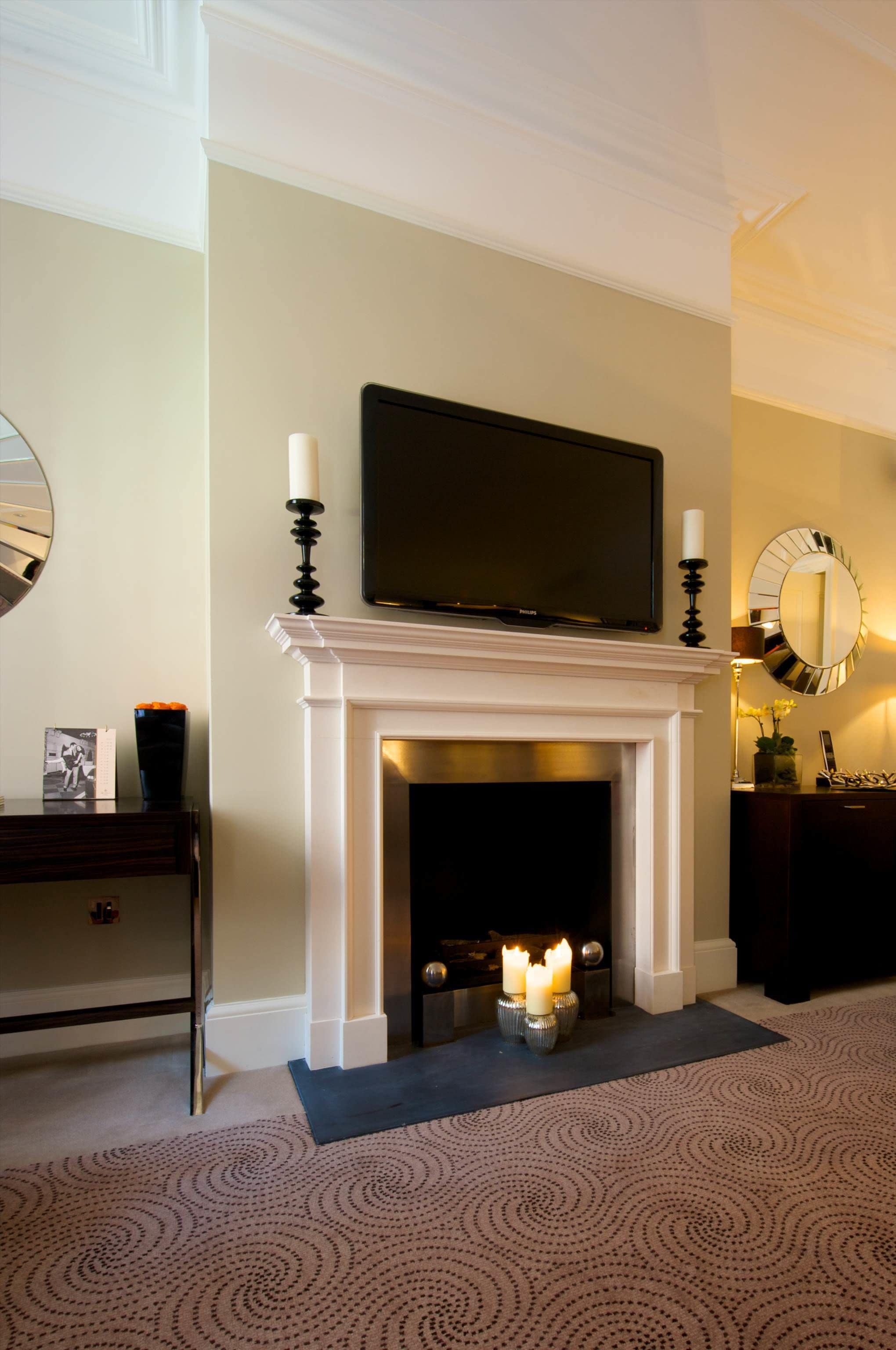 Una habitación con chimenea blanca, un televisor montado encima y un espejo en la pared.