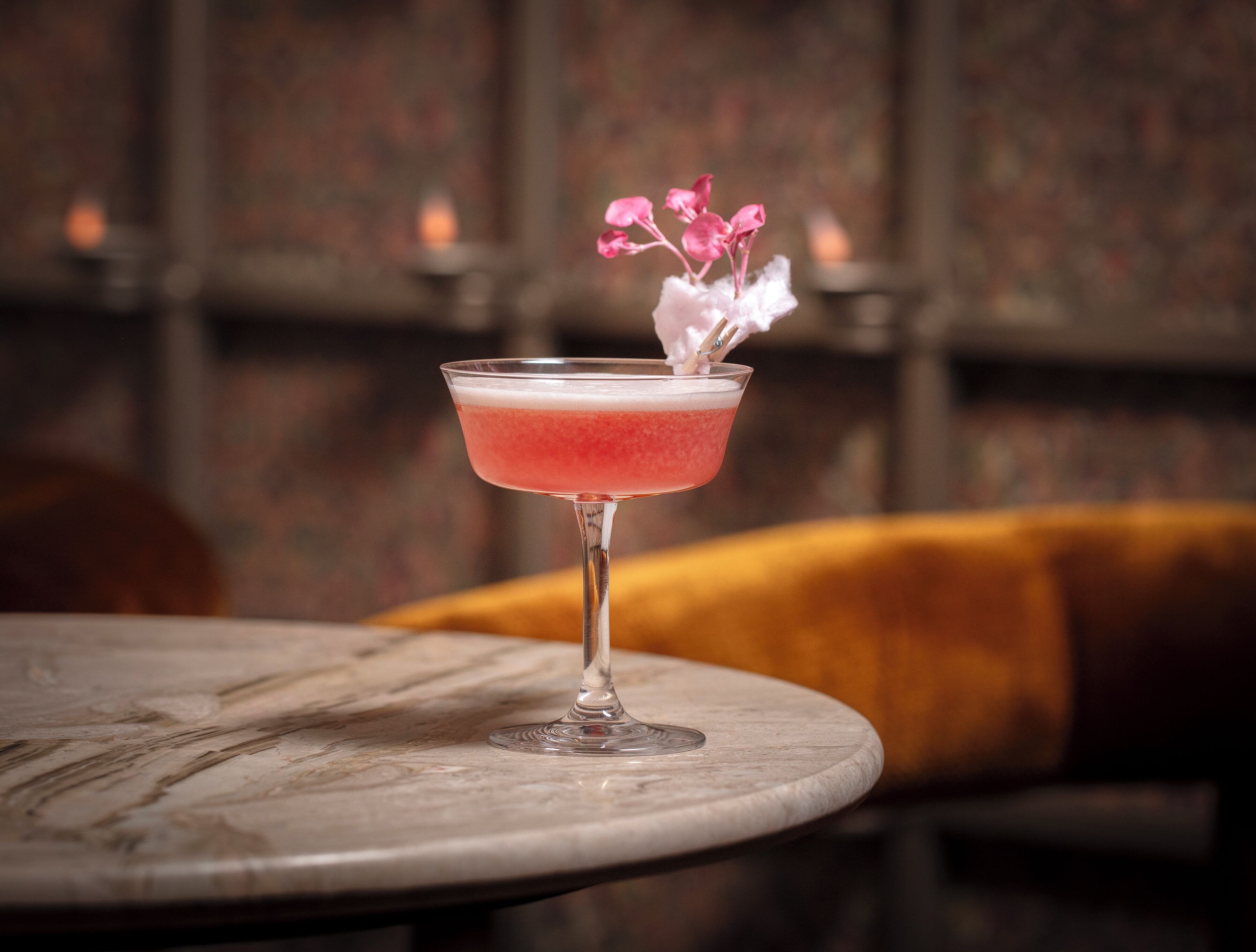 A cocktail in a martini glass on a marble table with a blurred background.