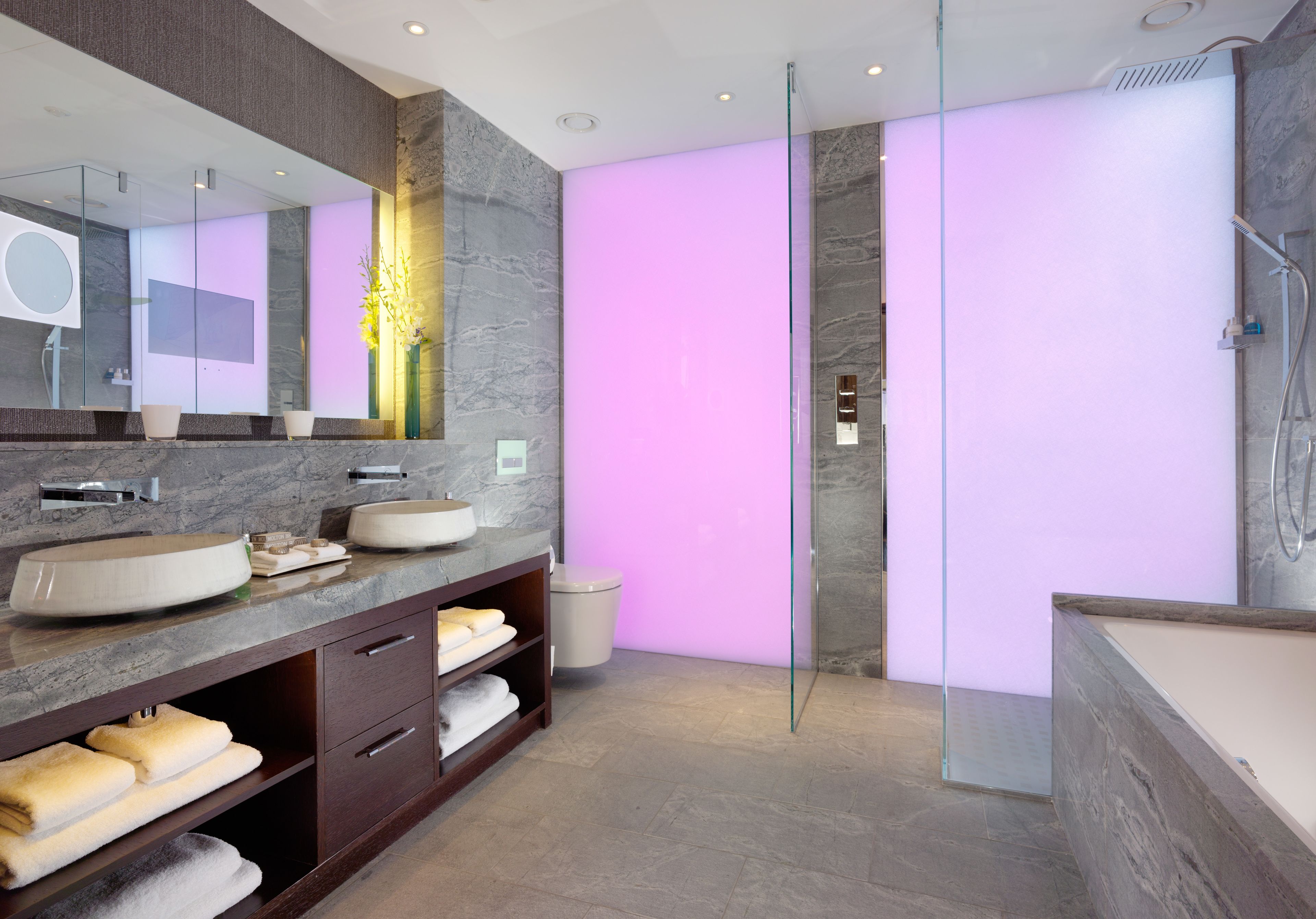 Een moderne badkamer met een grote spiegel, twee wastafels, een douche en een badmeubel met handdoeken.