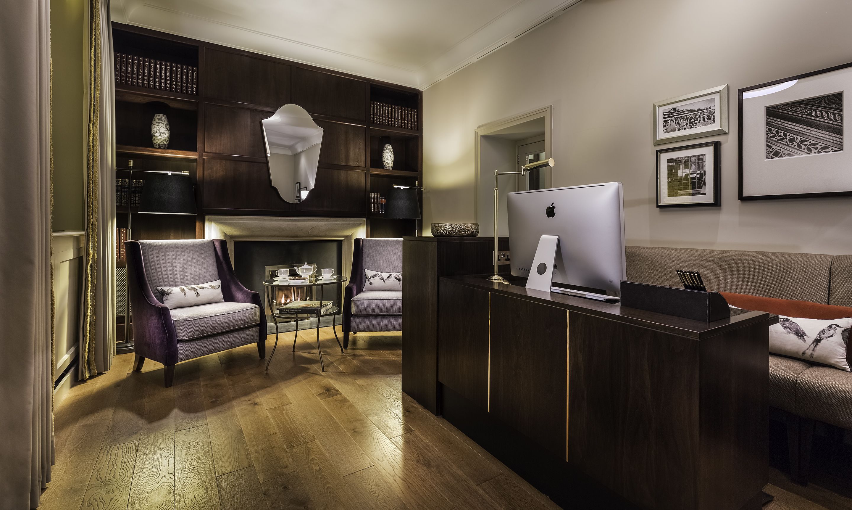 A modern living room with a fireplace, a sofa, two armchairs, a coffee table, and a desk with an Apple iMac.
