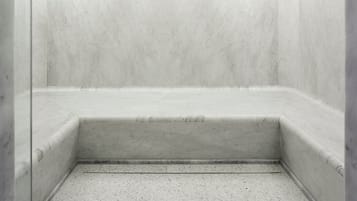 Un baño con paredes y suelo de mármol blanco, un rincón ducha y un escalón pequeño que conduce a la ducha.
