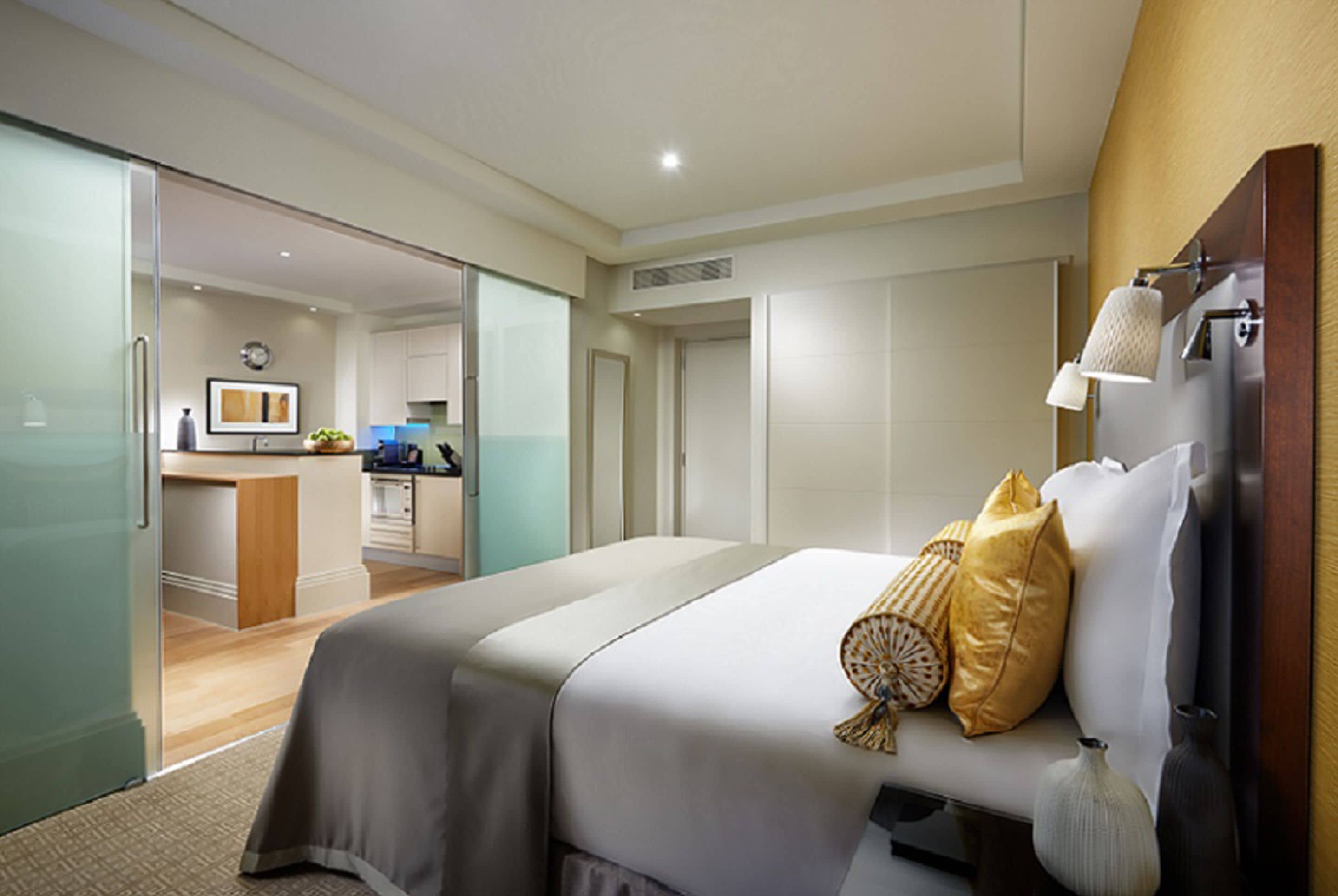 Een hotelkamer met een bed, nachtlampjes en uitzicht op de keuken en badkamer.