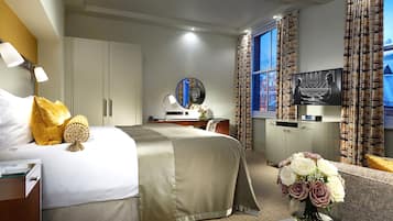 A hotel room with a bed, a desk, a television, and a vase of flowers.