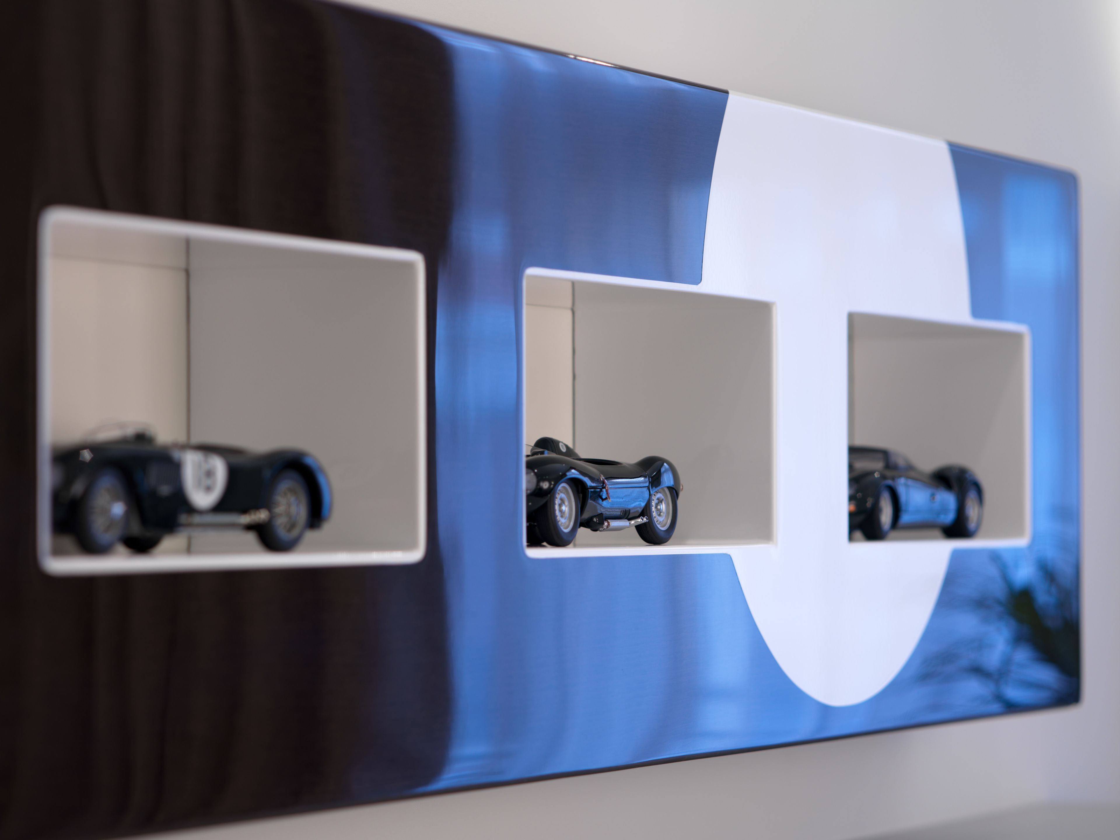 A wall with three rectangular display cases containing model cars.