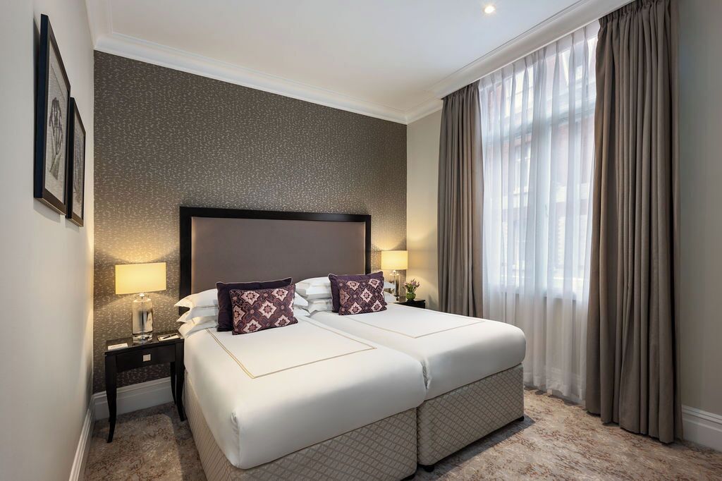 A double bed with a headboard, two bedside tables with lamps, a large window with curtains, and a textured wall.