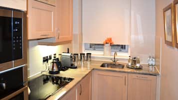 A modern kitchen with wooden cabinets, a built-in oven, a microwave, a coffee maker, and a window with a vase of flowers.