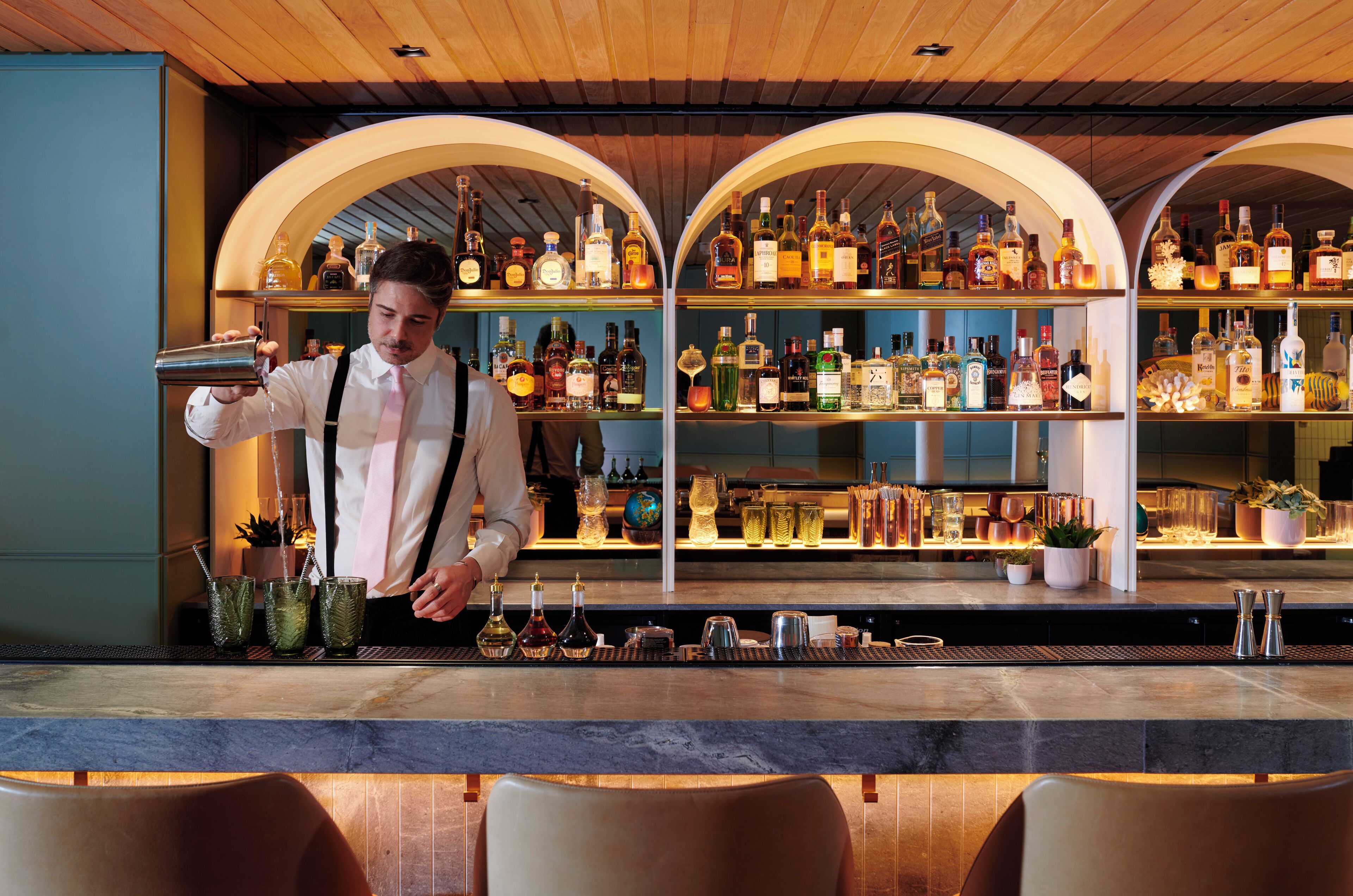 A bar area with shelves of liquor bottles, a bartender preparing drinks, and a bar counter.
