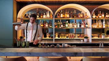 A bar area with shelves of liquor bottles, a bartender preparing drinks, and a bar counter.