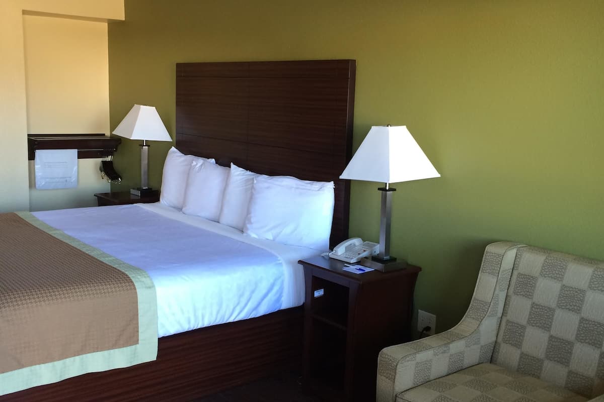 Una habitación de hotel con una cama, dos lámparas de noche, una silla, una mesita y un teléfono en la mesilla.