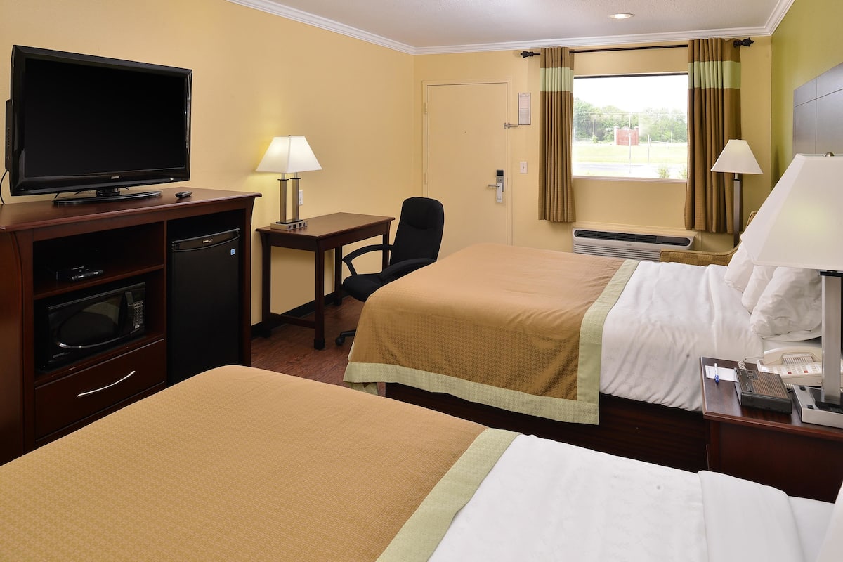 Habitación de hotel con dos camas, un televisor, un escritorio con silla y una ventana con cortinas.