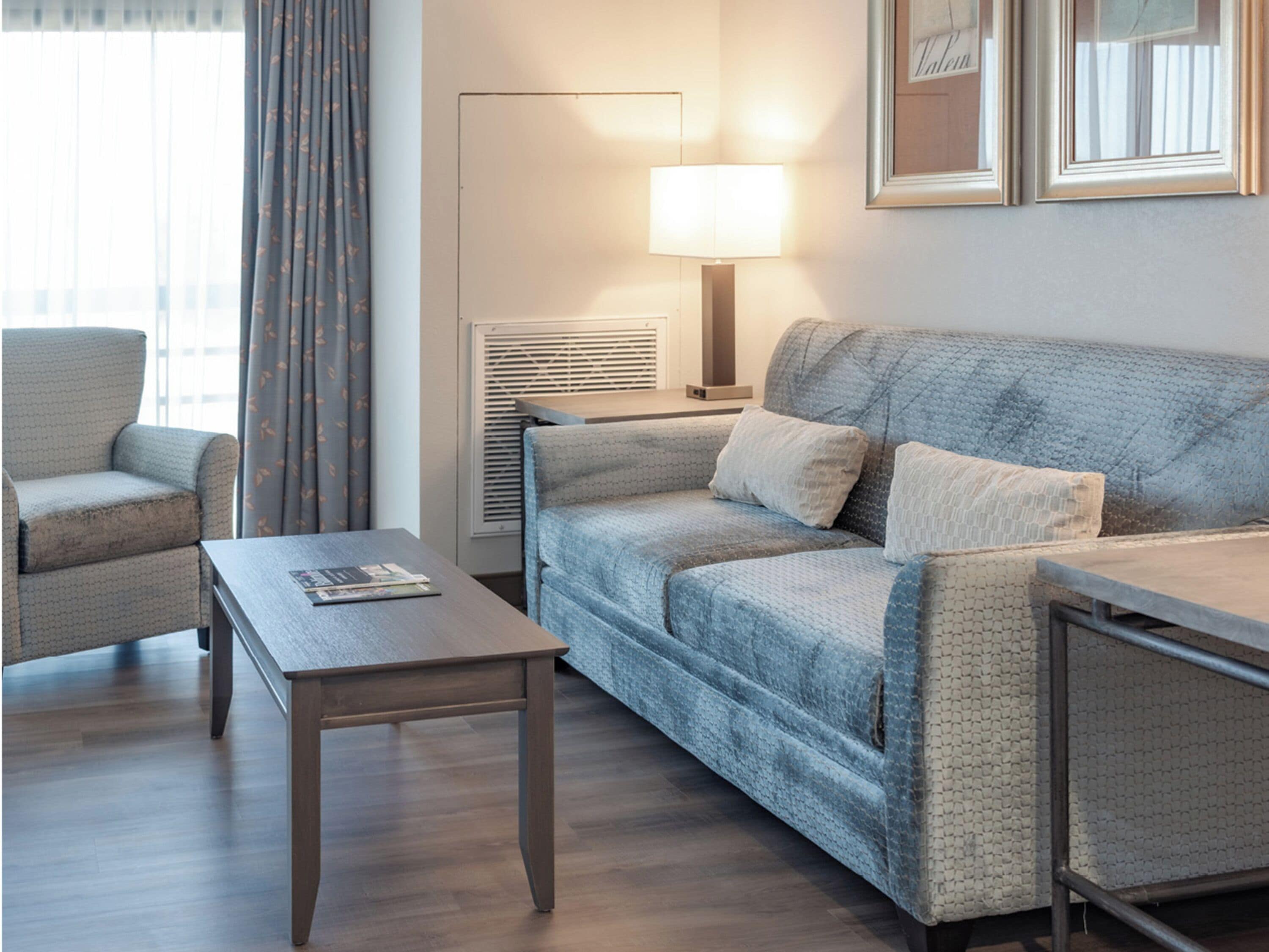 A hotel room with a sofa, armchair, and a small table.