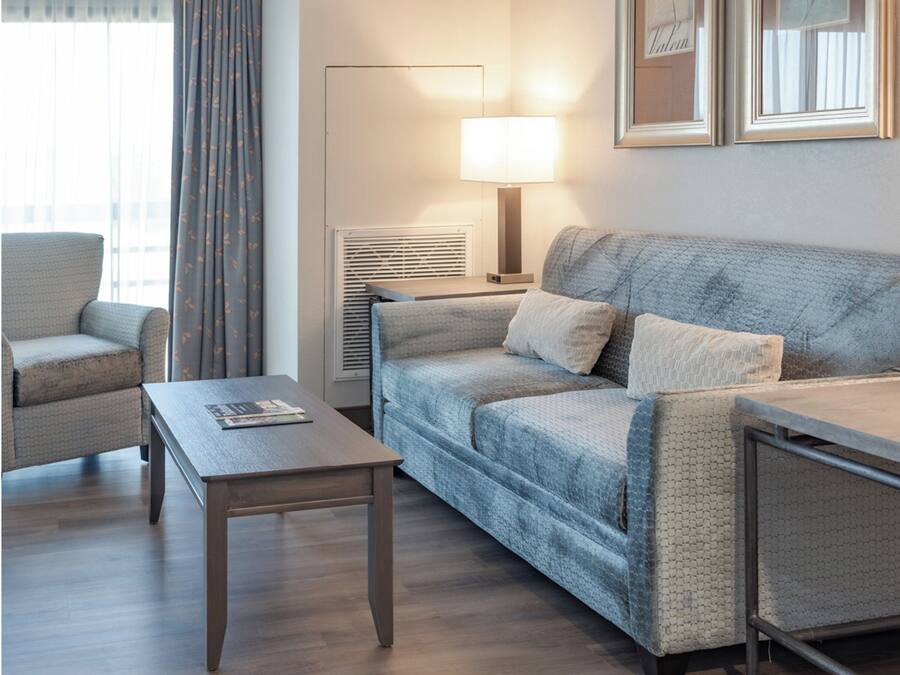 A hotel room with a sofa, armchair, and a small table.