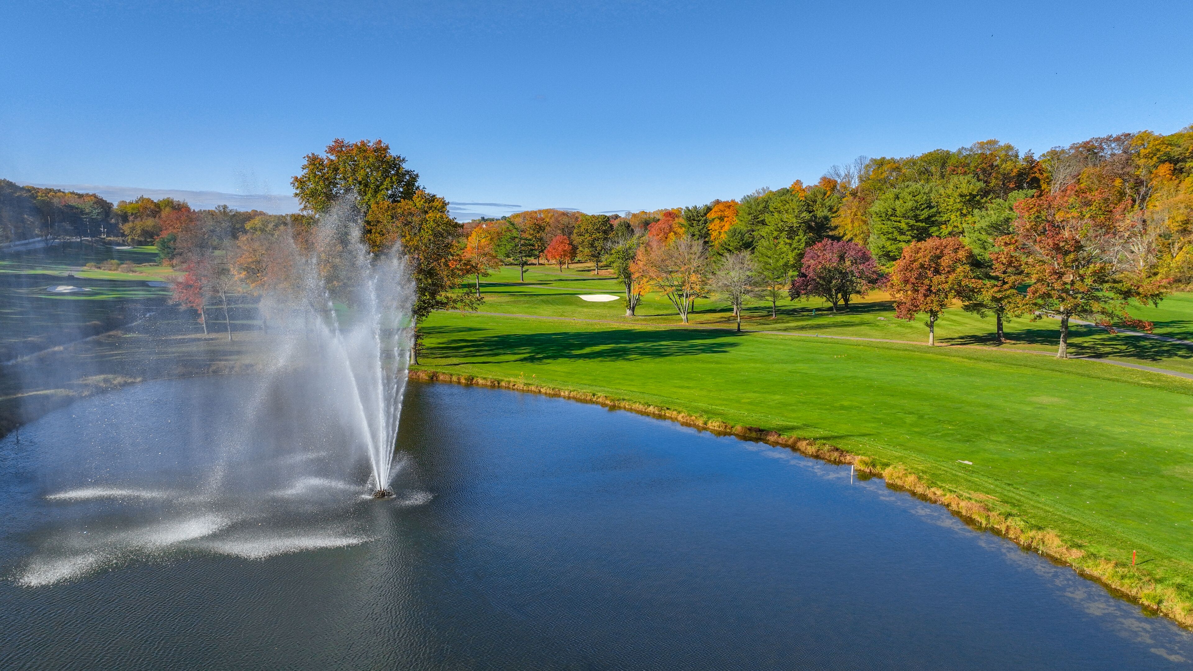 A golf course with a water feature and autumn-colored trees.