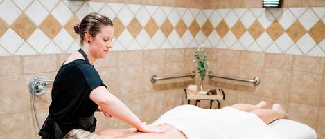 A massage therapy room with a massage table, a client lying face down, and a therapist performing a massage.