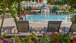 A pool area with lounge chairs and a table, surrounded by flowers and a building in the background. - Turf Valley Resort (Ellicott City)