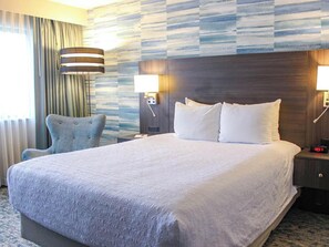 A hotel room with a large bed, two bedside lamps, a chair, and a wall with a striped pattern. - Turf Valley Resort (Ellicott City)