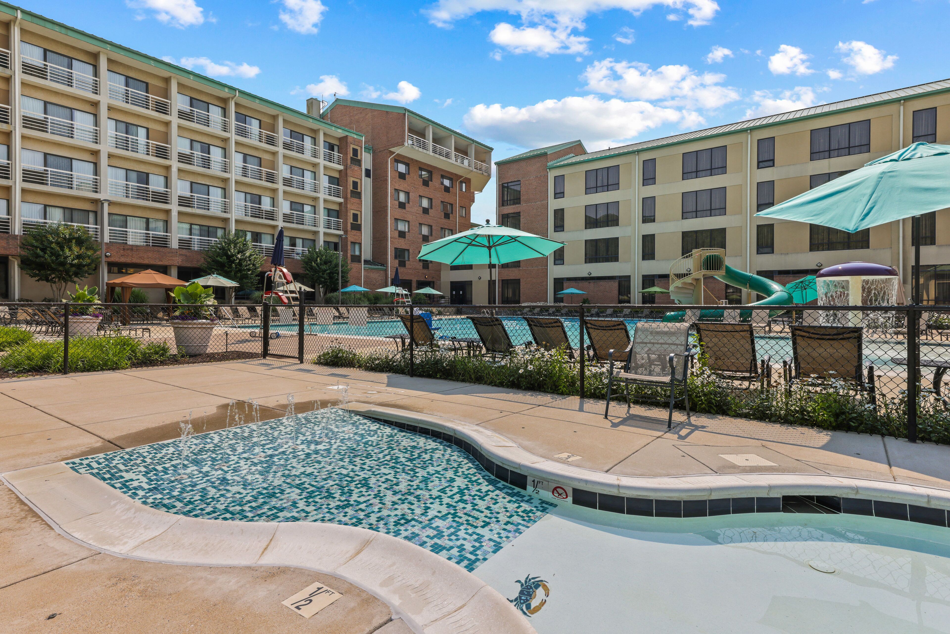 A swimming pool area with lounge chairs and umbrellas, surrounded by a fence.