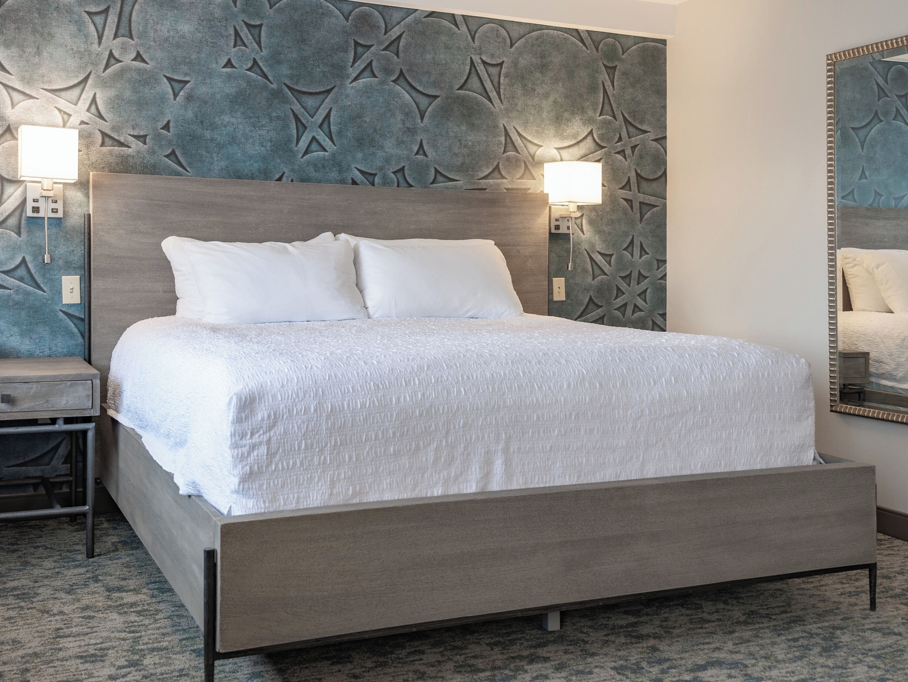 Una habitación de hotel moderna con una cama grande, dos lámparas de noche y un panel decorativo en la pared.