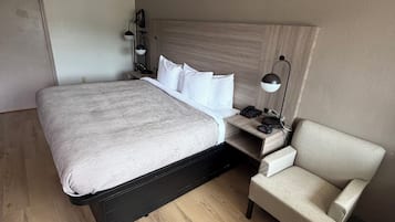 Una camera d'albergo con un letto grande, un comodino con una lampada, una sedia e un termosifone.